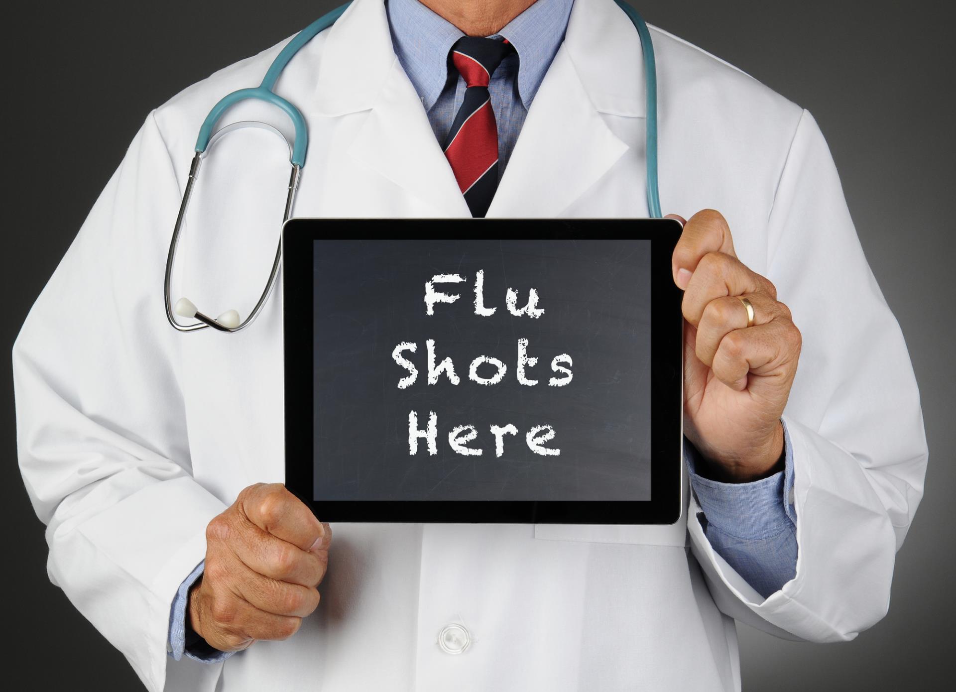 Doctor holding flu shots here sign