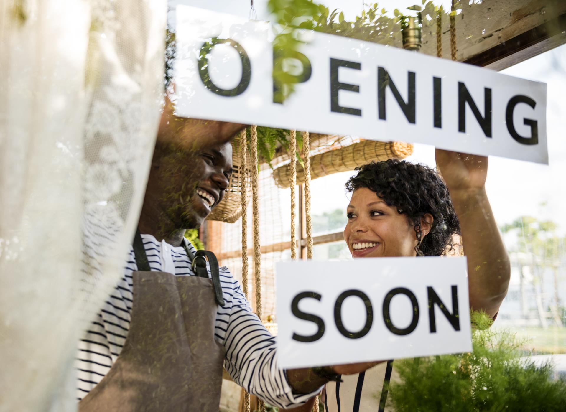 Store owners displaying a sign that reads opening soon in the window at their business